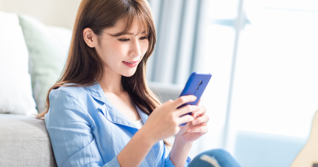 ソファに座りながらスマートフォンを使用する女性