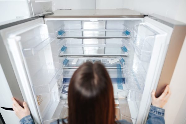 Young attractive woman choosing refrigerator in hypermarket close up